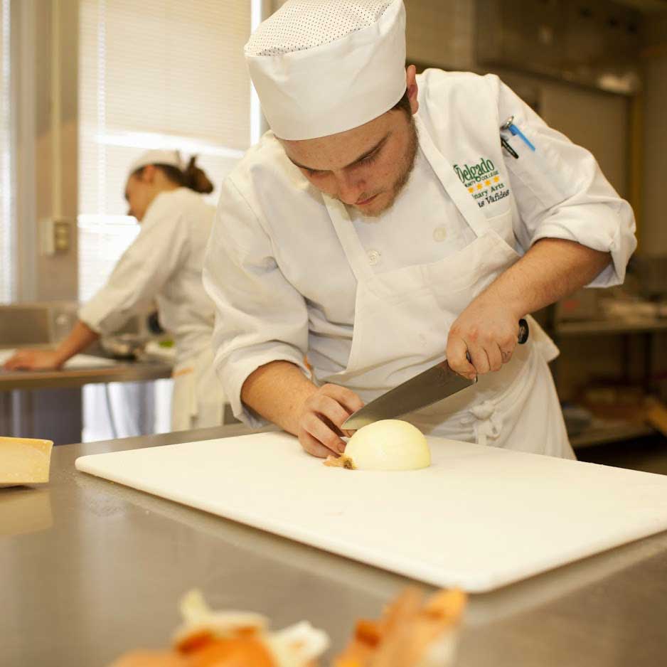 A Delgado culinary arts student cuts an onion.