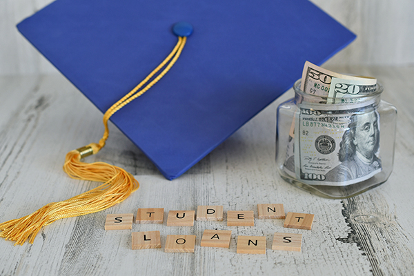 graduation cap with a jar filled with money and scrabble blocks that spell out "student loans"