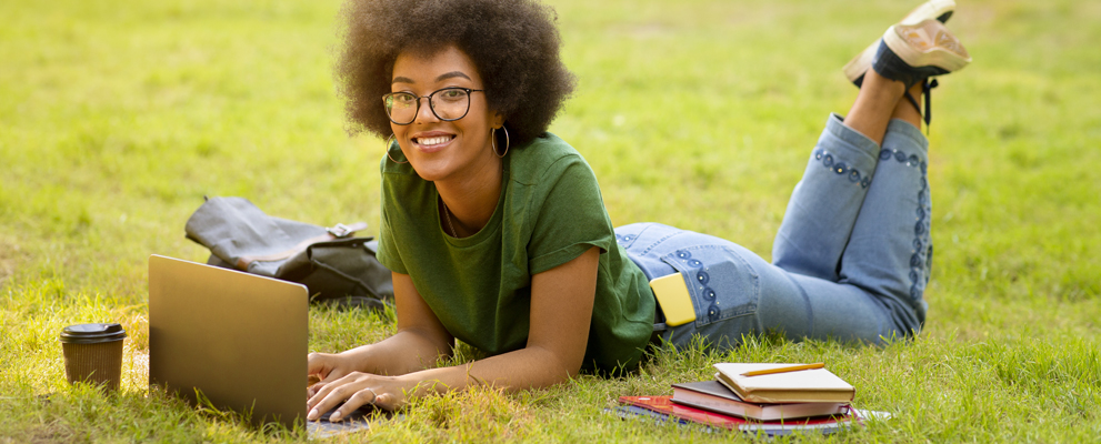 black college student studying, laying on lawn