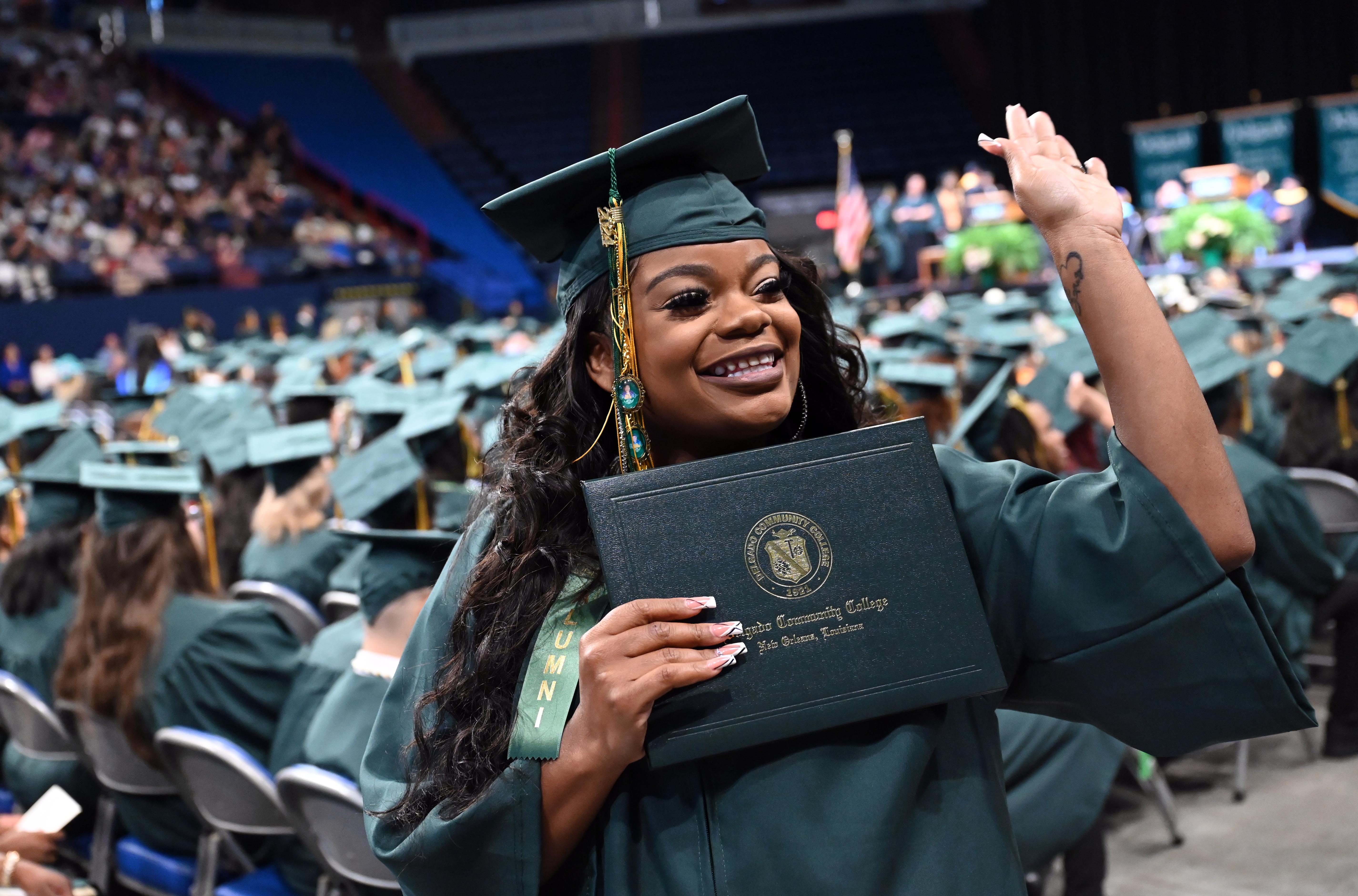 A graduate waves to the crowd while holding a diploma cover